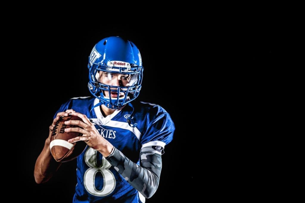 man holding football and football uniform in black background